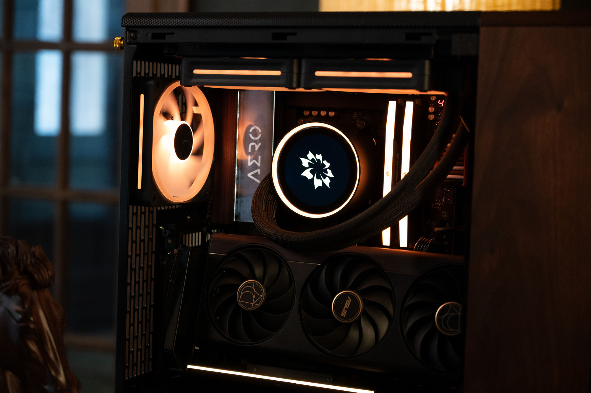 The Gigabyte X870E AERO motherboard in a wood-toned finish, beside the flower-emblem pump and glowing memory