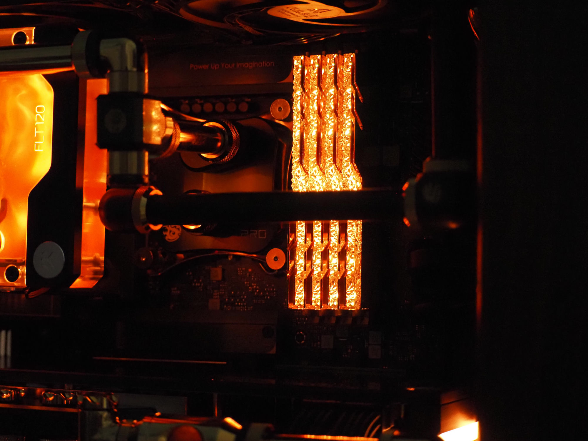 A dark Optimist build lit in deep amber — EK “FLT120” reservoir, hardline tubing and glowing memory