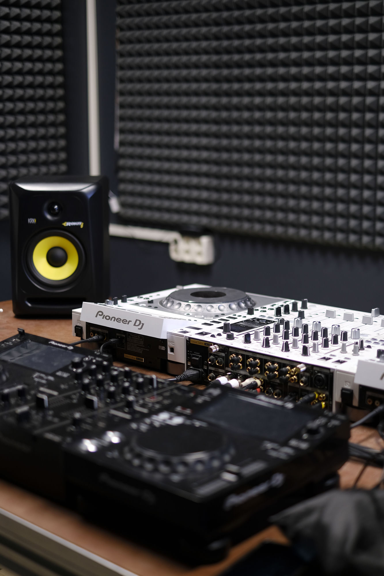 A studio corner — acoustic foam panels on the wall, a KRK studio monitor and Pioneer DJ decks