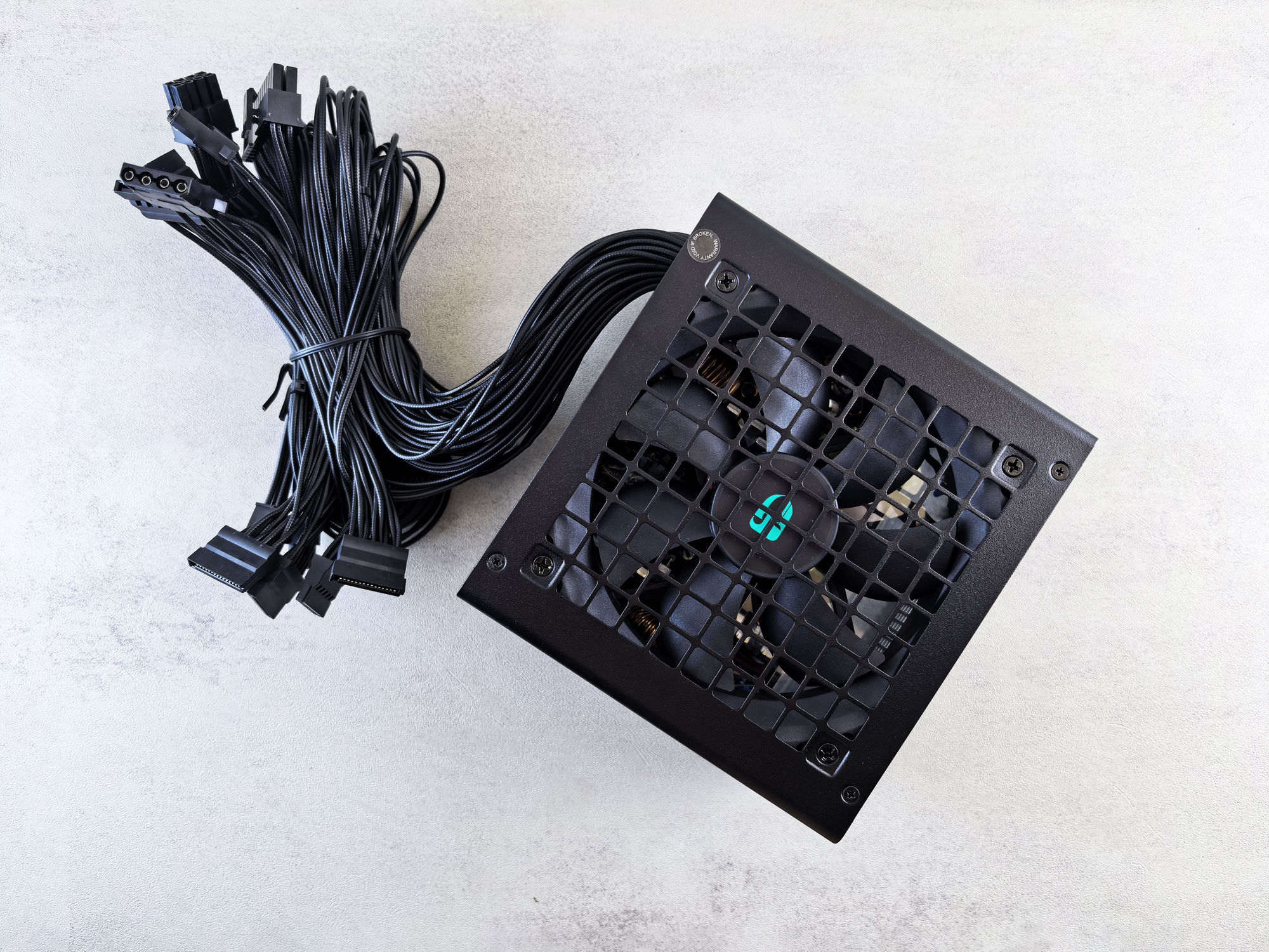 A black modular power supply unit beside a coil of black sleeved cables, shot top-down on a light concrete surface