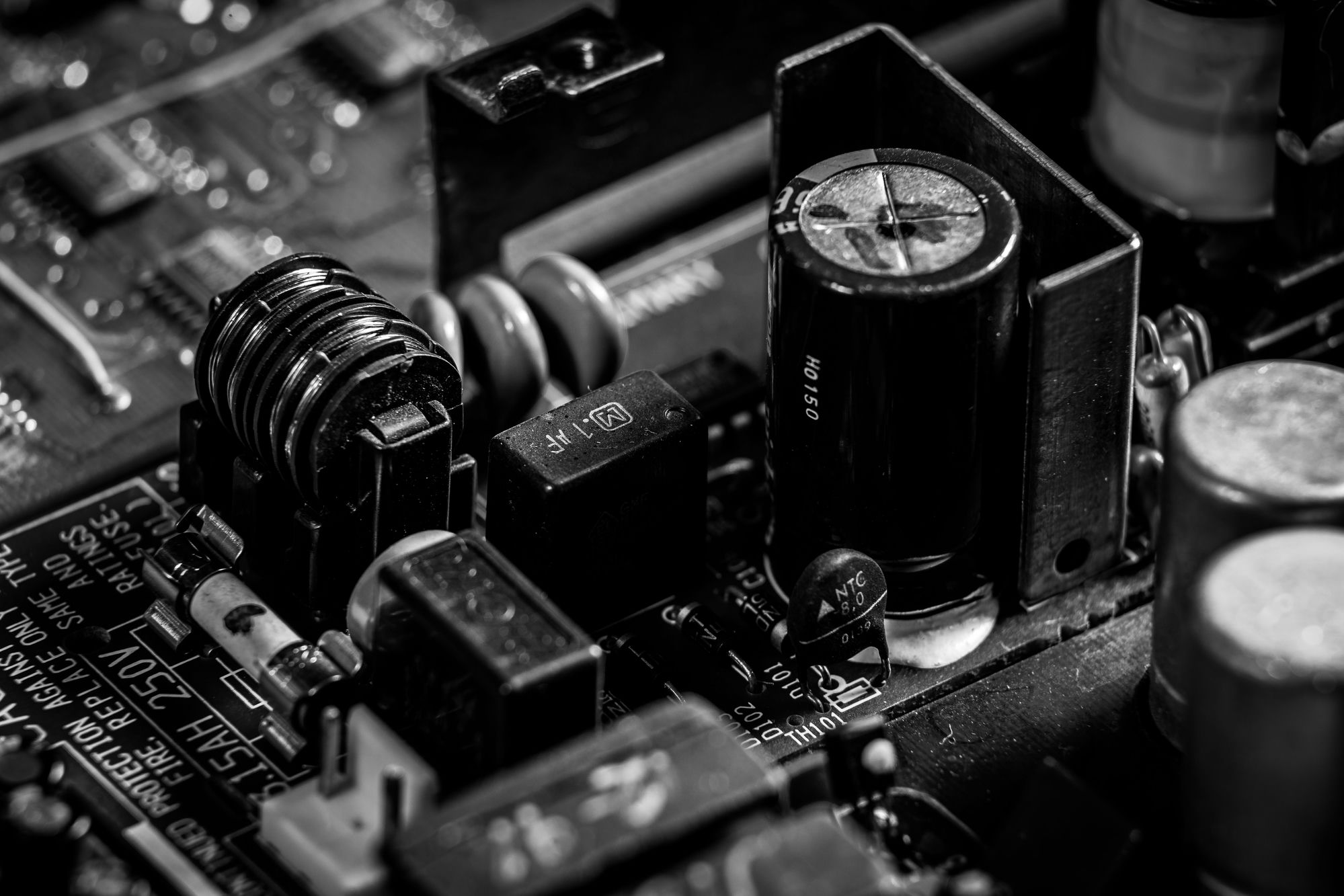 A black-and-white macro of a power supply’s internals — capacitors, a fuse, an NTC thermistor and a fire-protection label