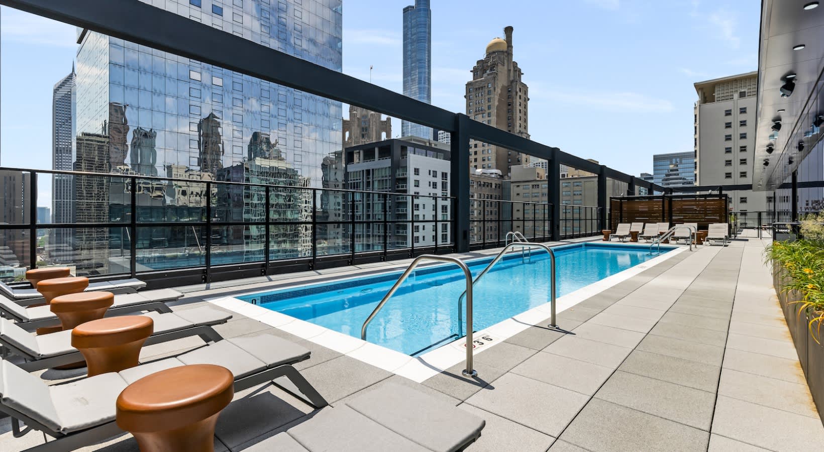 Rooftop pool with metal railing, lounge chairs with orange cushions, and Chicago skyline backdrop.
