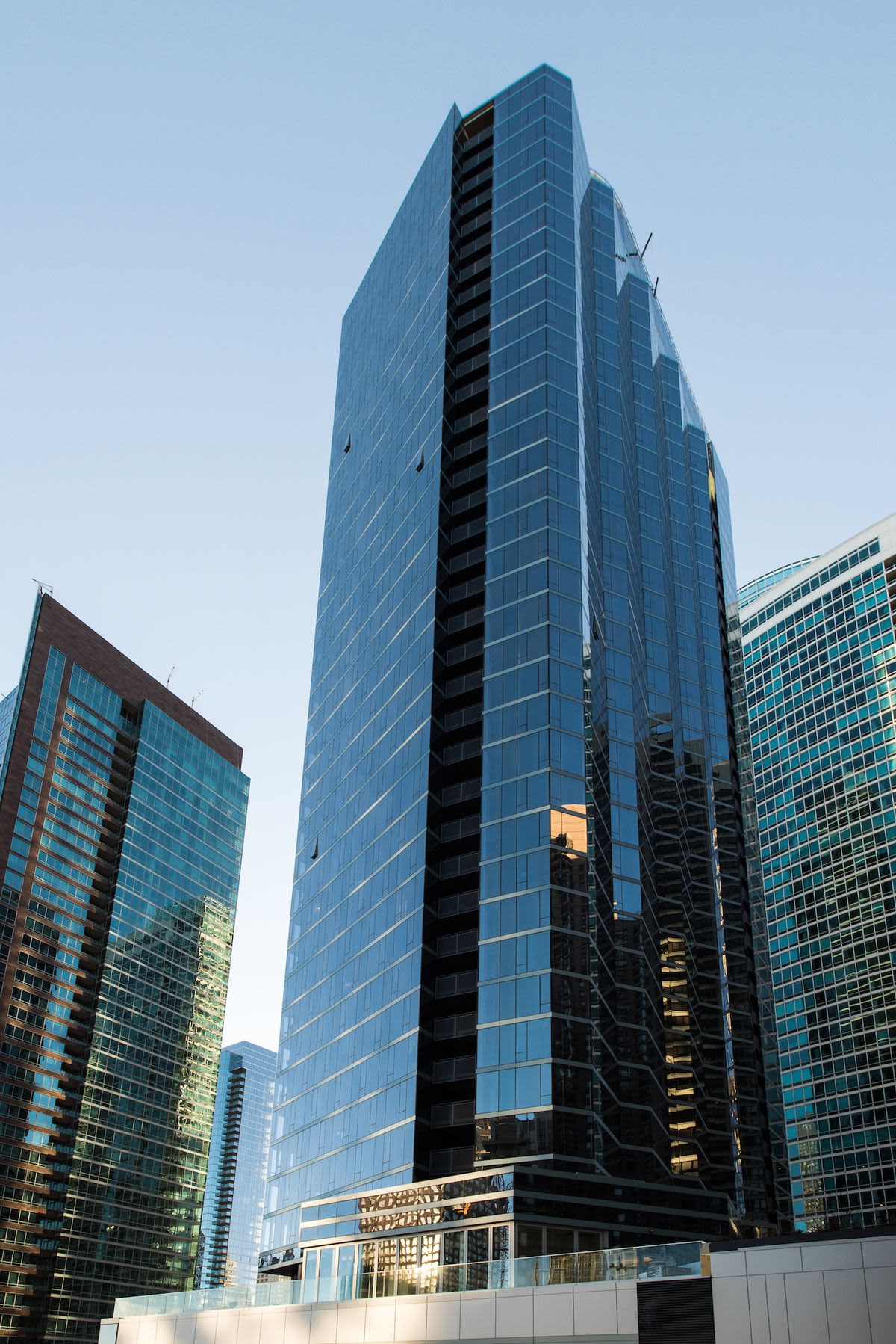 Contemporary glass and steel high-rise apartment tower with reflective blue facade and dark balconies against clear sky.