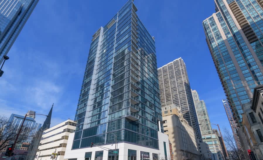 Modern glass and steel high-rise residential tower surrounded by other downtown Chicago buildings under clear blue sky.