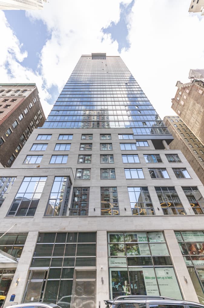 Tall residential tower with glass and metal facade, retail storefronts at street level, surrounded by historic buildings.