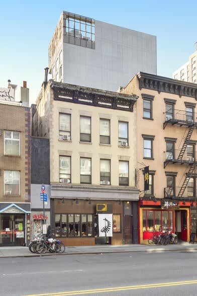 Modern white loft building with large windows above historic brick storefronts and street-level shops in New York City.