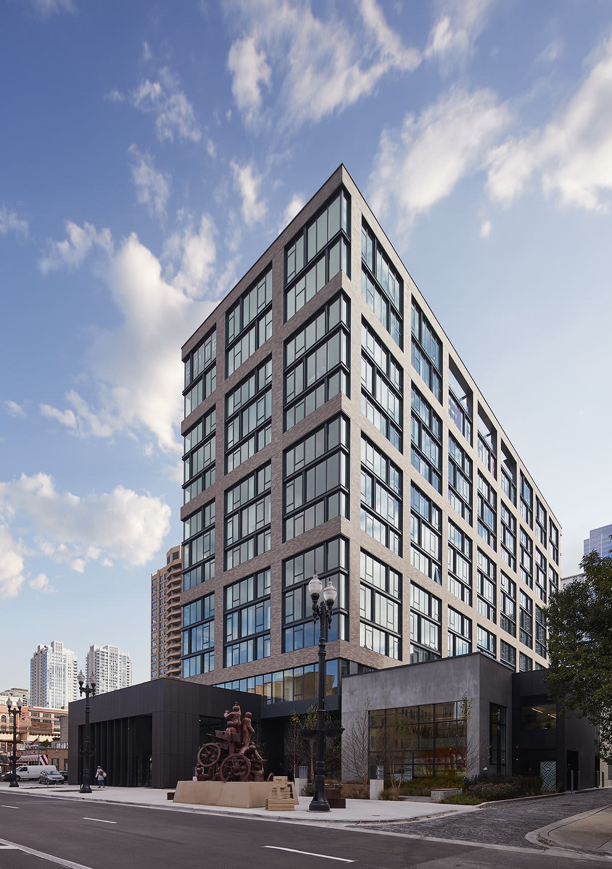 Contemporary residential building with red brick facade, large gridded windows, and dark ground-level retail space with sculptural art.