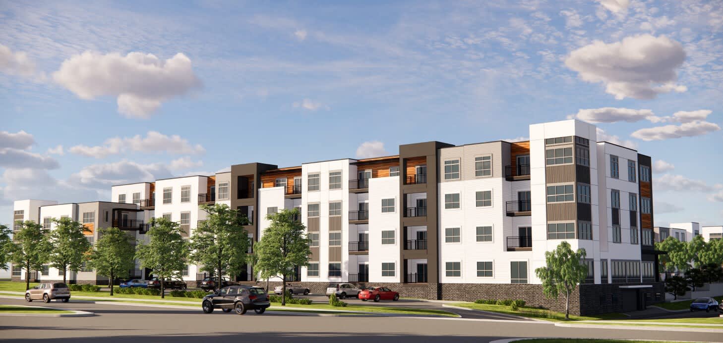 Modern apartment complex with white and bronze exterior, multiple stories, large windows, and landscaped grounds along street.