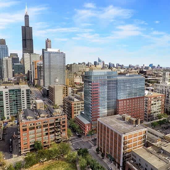 Elevated view of Chicago West Loop neighborhood with Willis Tower, modern high-rise buildings, and tree-lined streets under blue sky.