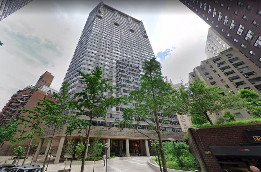 Tall residential tower with horizontal striping, ground-level brick entrance, mature trees in courtyard, surrounded by other city buildings.
