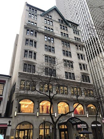 Historic gray stone building facade with arched storefronts at street level and rows of windows on upper floors.