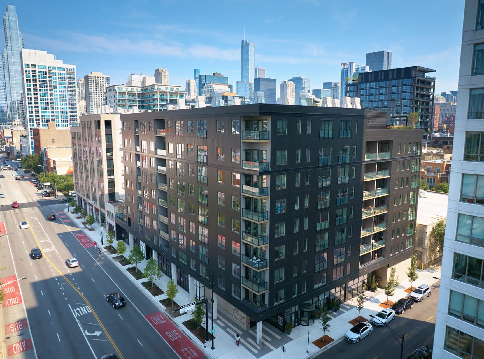 Dark brick apartment building with green-tinted windows overlooking a Chicago street, with downtown skyscrapers visible in the background.