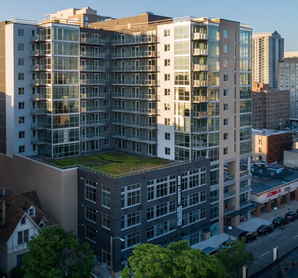 Modern multi-story residential building with glass balconies, green rooftop terrace, and ground-level retail in downtown Milwaukee.