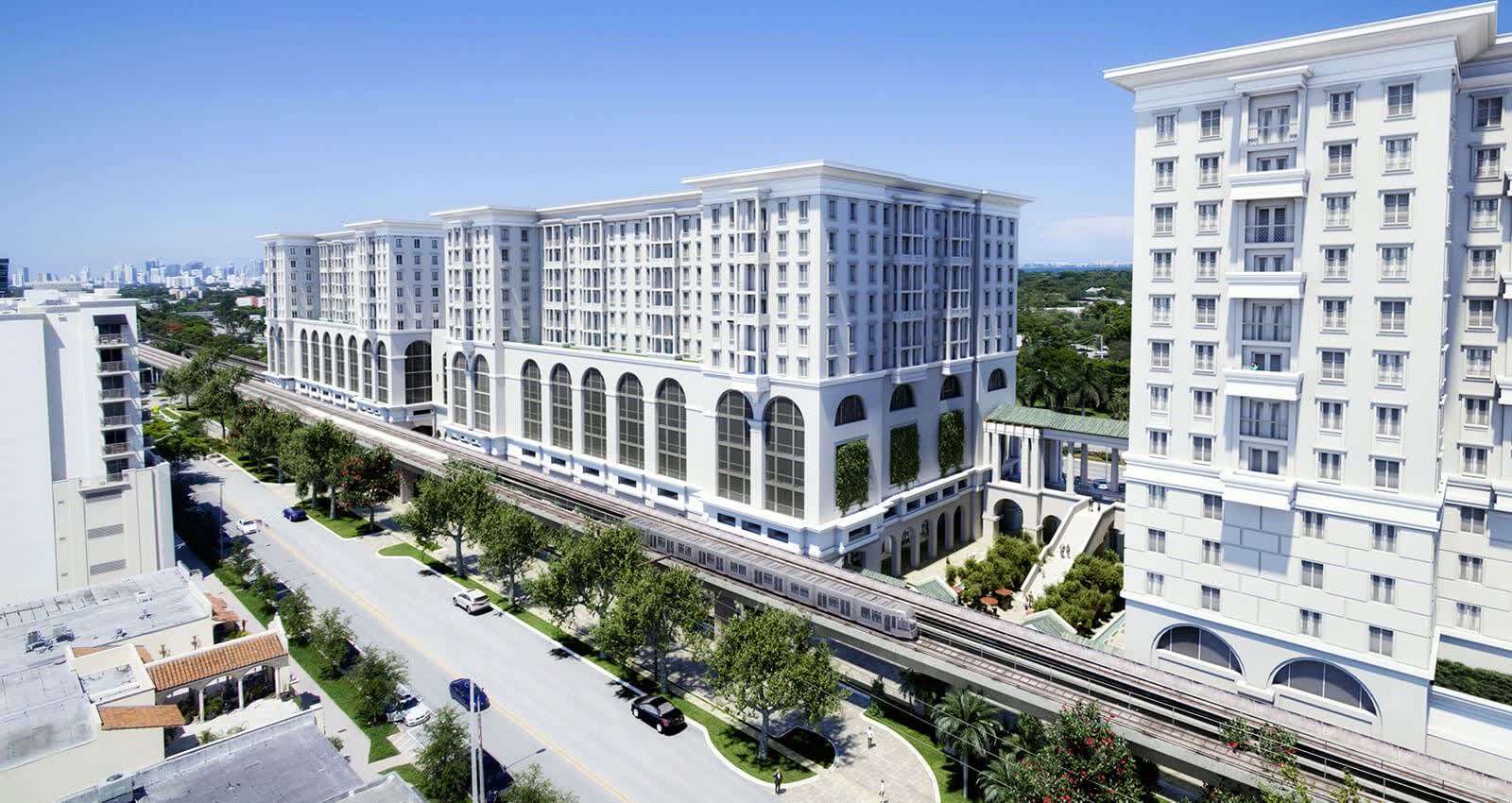 Multi-story white residential building with arched ground-floor colonnade, surrounded by landscaped streets and adjacent apartment towers under clear sky.