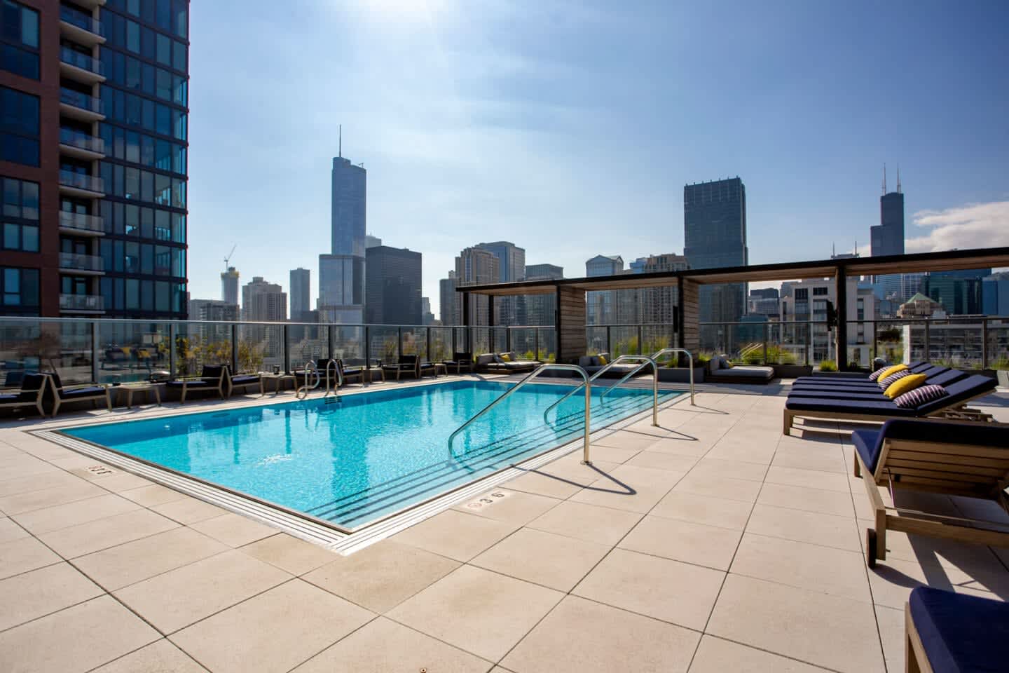 Rooftop swimming pool with glass railings, lounge chairs, and Chicago skyline in background.