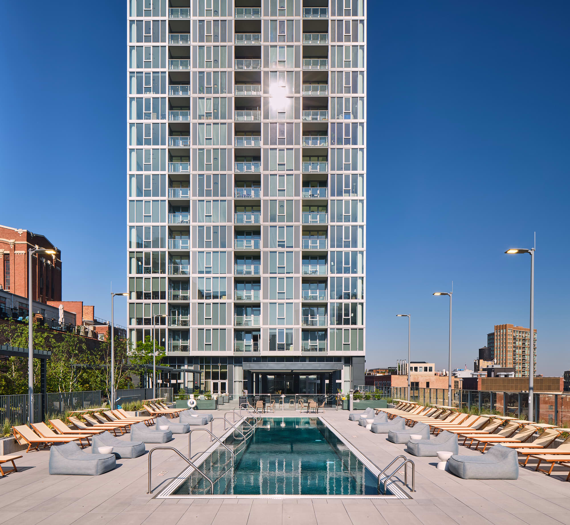 Rooftop pool surrounded by lounge chairs and white seating pods, with a modern high-rise building and Chicago skyline in the background.