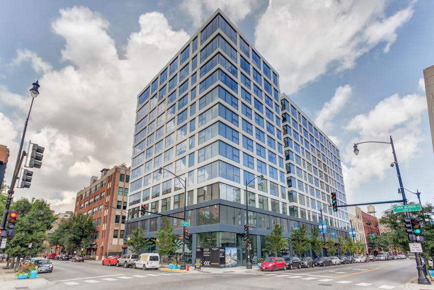 Modern multi-story residential building with blue-tinted glass windows and gray facade on a Chicago street corner with retail at ground level.