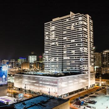 Illuminated high-rise residential tower at night with glass base retail level and surrounding Chicago cityscape.