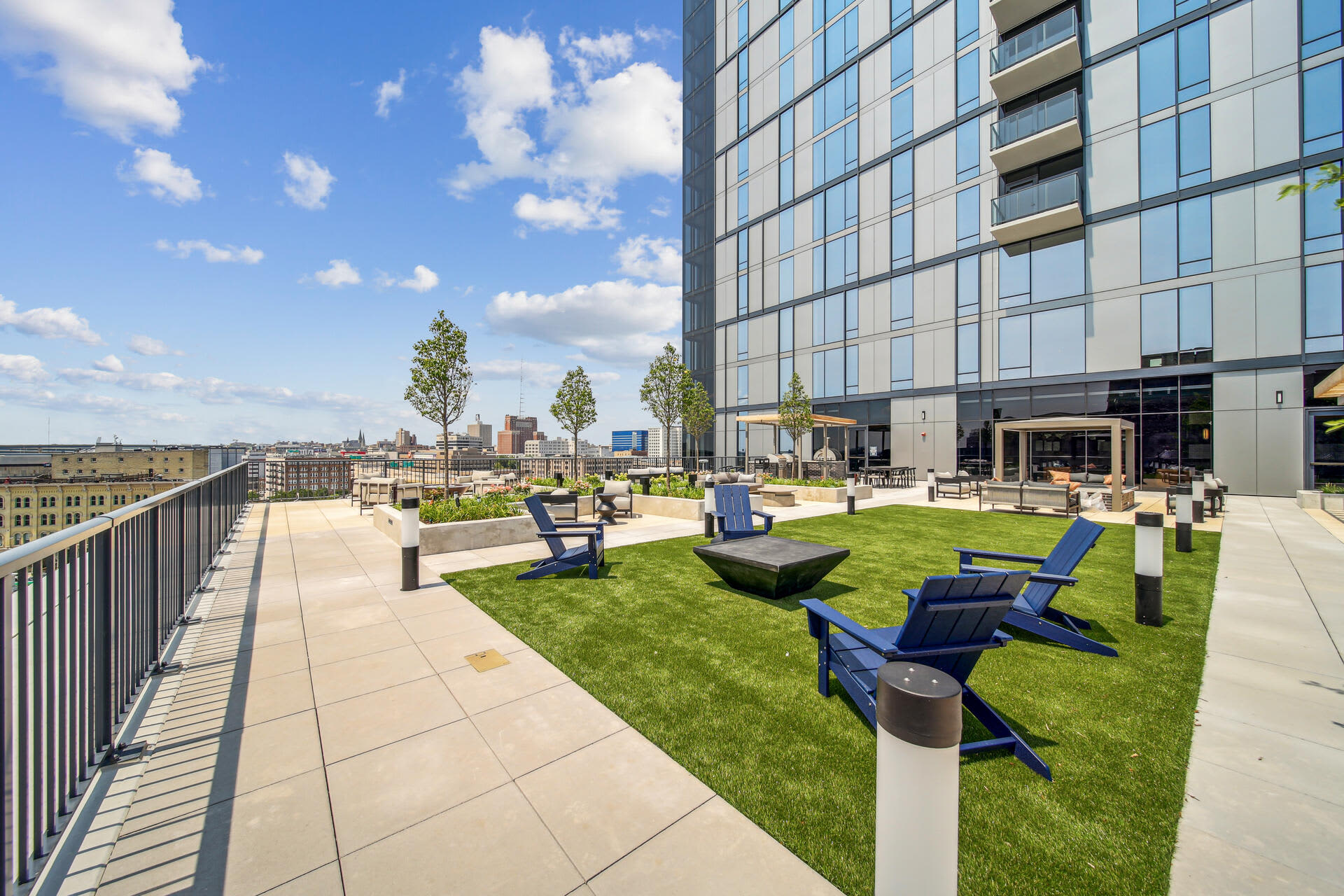 Rooftop terrace with green lawn, blue Adirondack chairs, concrete patio, and downtown Milwaukee skyline view.