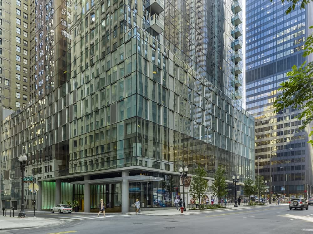 Modern glass-facade building with ground-level retail entrance, surrounded by tall office towers on an urban Chicago street.