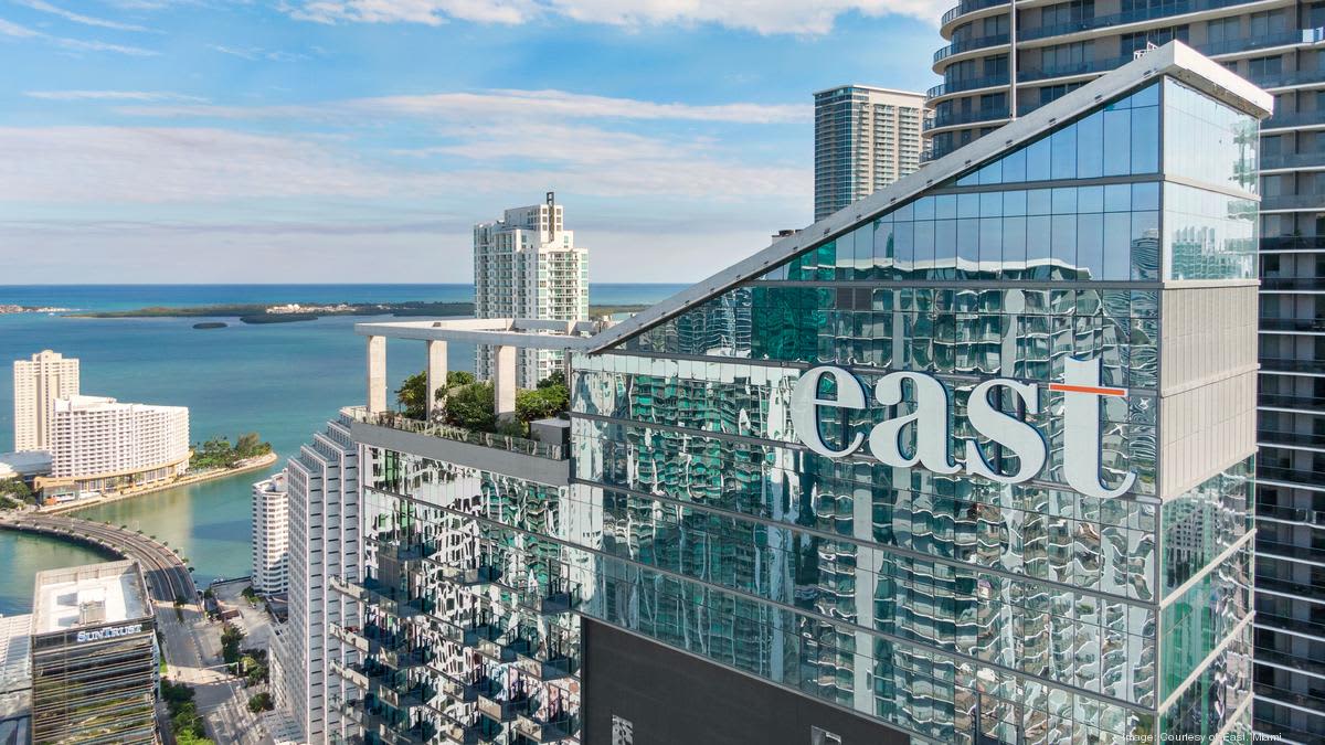High-rise balcony with glass railing overlooking Biscayne Bay, downtown Miami buildings, and waterfront cityscape under blue sky.