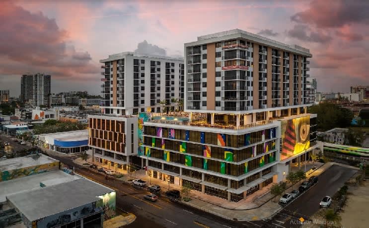 Modern mixed-use building in Miami with residential towers above colorful ground-floor retail space and street-level storefronts at dusk.