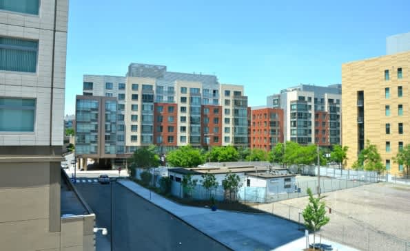 View from residential building overlooking courtyard with surrounding multi-story apartment buildings in various colors and clear sky.