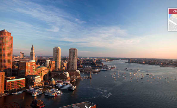 Boston waterfront at sunset with downtown skyline, harbor with sailboats, and historic buildings in warm light.