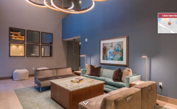 Modern living room with blue accent wall, tan and mint seating, wood coffee table, neon ceiling fixture, and framed artwork.