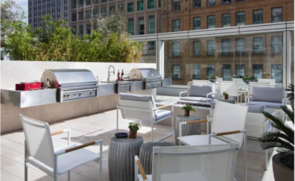 Rooftop terrace with stainless steel grills, gray lounge chairs, and downtown San Francisco skyline in background.