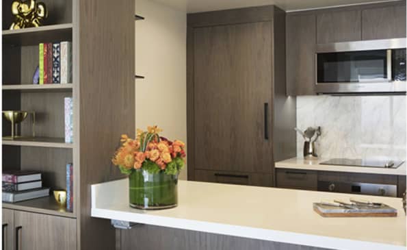 Modern kitchen with white quartz island, dark wood cabinetry, built-in shelving with books and decor, and orange flowers in a vase.