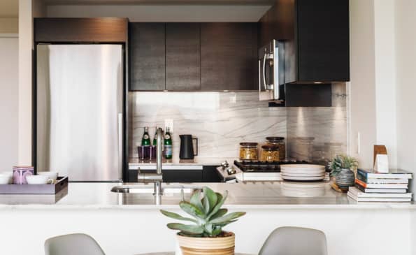 Modern kitchen with dark wood cabinets, white marble backsplash, stainless steel refrigerator, and white countertop with dining seating for two.