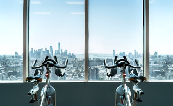 Two stationary bikes in a bright fitness room with expansive windows framing the New York City skyline.