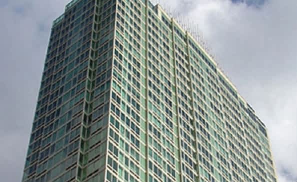 Tall residential high-rise building with green-tinted glass facade and regular window pattern against cloudy sky.