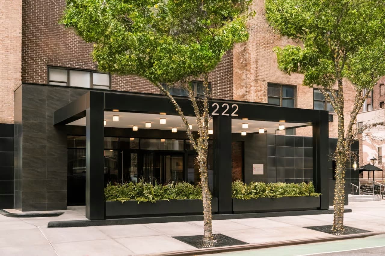 Modern black storefront with address 222, large windows, planters with greenery, and ivy-covered brick building behind.