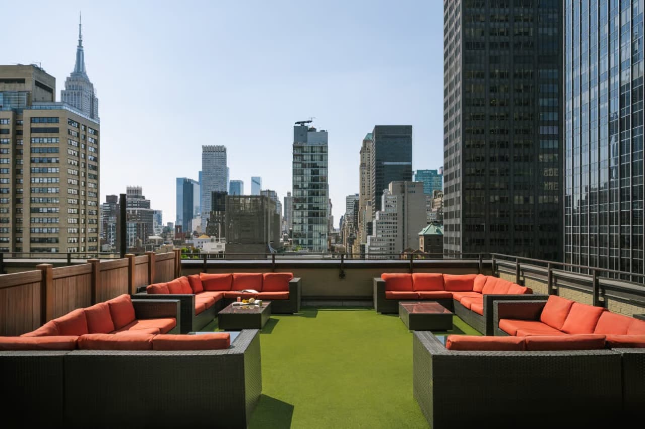 Rooftop lounge with orange modular seating, artificial green turf, and Manhattan skyline backdrop featuring the Chrysler Building.
