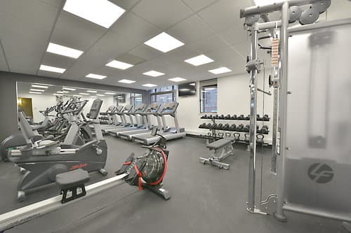 Modern gym with stationary bikes, treadmills, dumbbells, and cable machine under bright ceiling lights.