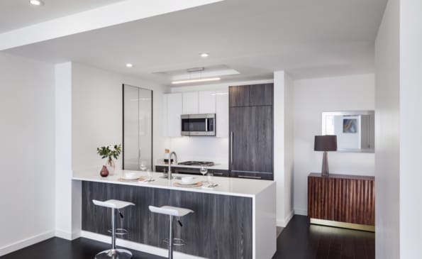 Modern kitchen with dark wood cabinetry, white countertops, breakfast bar with two white stools, and stainless steel appliances.