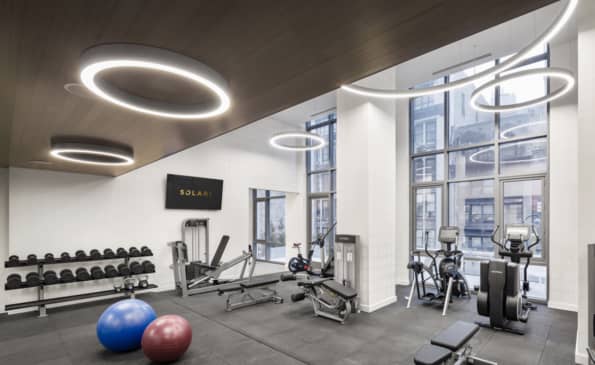 Fitness center with dumbbell rack, exercise bikes, treadmills, blue and pink stability balls, and floor-to-ceiling windows with city views.