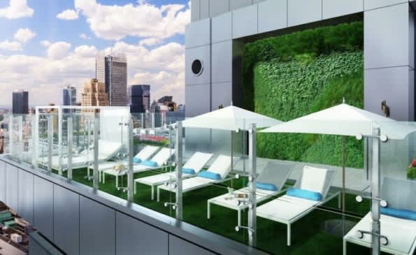 Rooftop terrace with white lounge chairs, umbrellas, green living wall, and downtown skyline view.