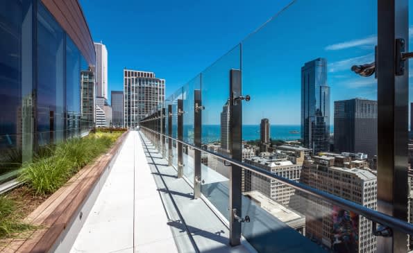 High-rise rooftop terrace with glass railing, wooden planter boxes, and expansive views of Chicago's downtown skyline and Lake Michigan.