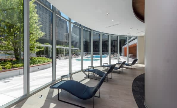 Modern lounge with black chaise lounges, floor-to-ceiling windows, and view of courtyard with pool and greenery.