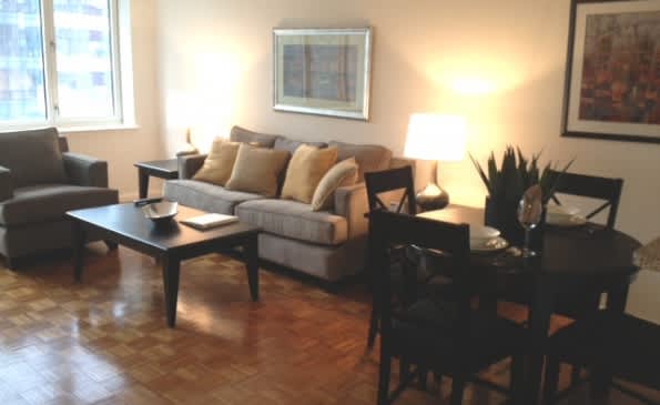 Living room with gray sofa, black armchair, wooden coffee table, hardwood floors, and large windows with city views.