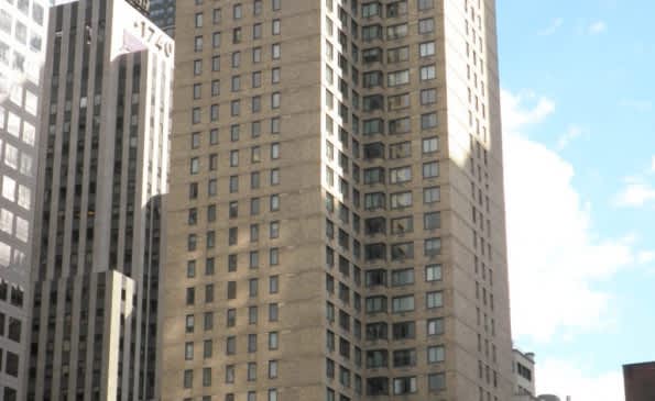 Exterior view of tall residential building surrounded by other downtown Manhattan skyscrapers under blue sky.