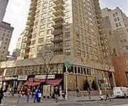 Tall residential building with ground-level storefronts and pedestrians on an urban street.