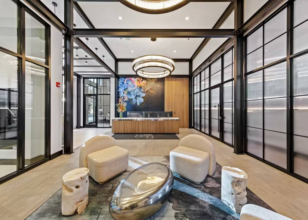 Contemporary lobby with cream-colored curved seating, polished metal sculptural elements, black-framed glass walls, and wood reception desk.