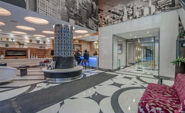 Modern hotel lobby with geometric black and white floor pattern, blue cylindrical column, curved reception desk, and contemporary furnishings.