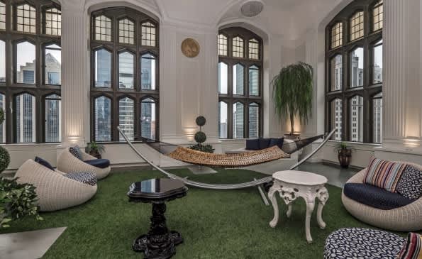 Recreation room with artificial grass floor, two hanging hammocks, bean bag seating, large arched windows, and city views.