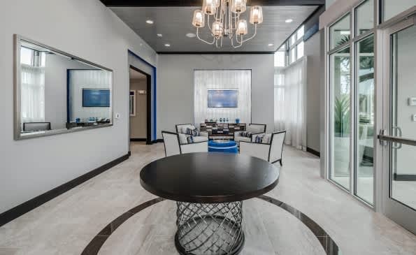 Modern clubhouse with round black table, contemporary chairs, pendant lighting, and glass doors opening to outdoor space.