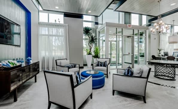 Modern leasing lounge with gray upholstered chairs, blue ottoman, floor-to-ceiling windows, and contemporary decor in neutral tones.